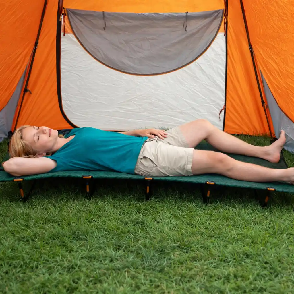 Blonde woman relaxing on a camping cot inside an orange tent set up on grass