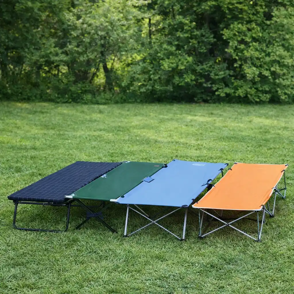 Four portable camping cots arranged on grass at an outdoor campsite