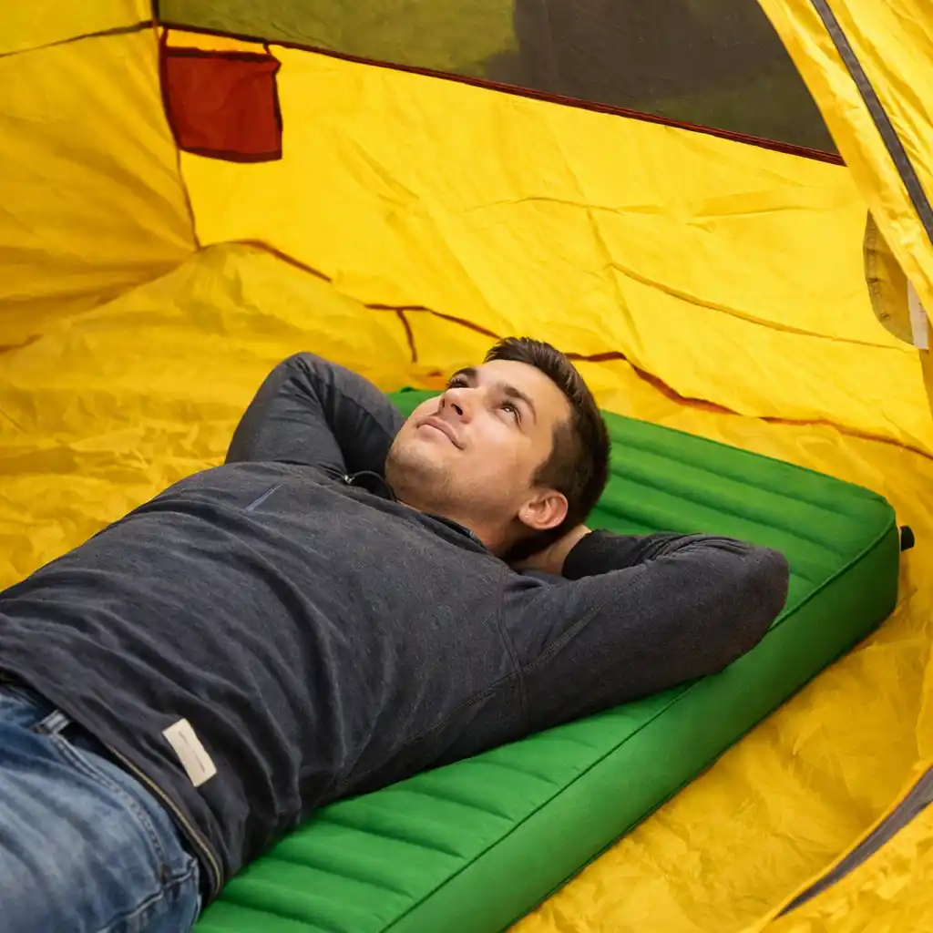 Man lying on a green sleeping mat inside a yellow camping tent
