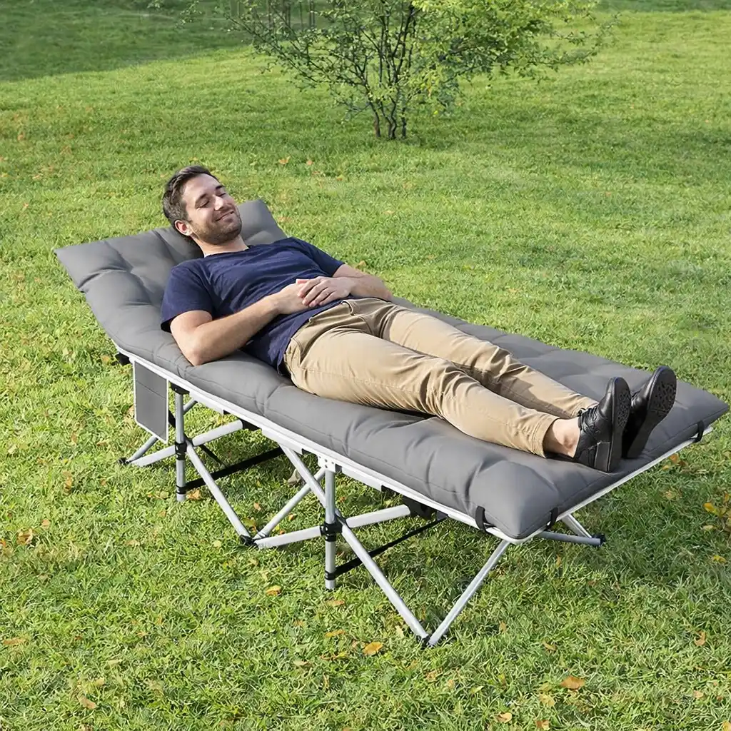 Man relaxing on a padded camping cot in a grassy outdoor setting