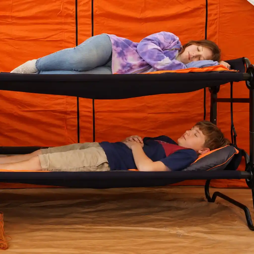 Two teenagers sleeping on camping bunk cots inside bright orange tent