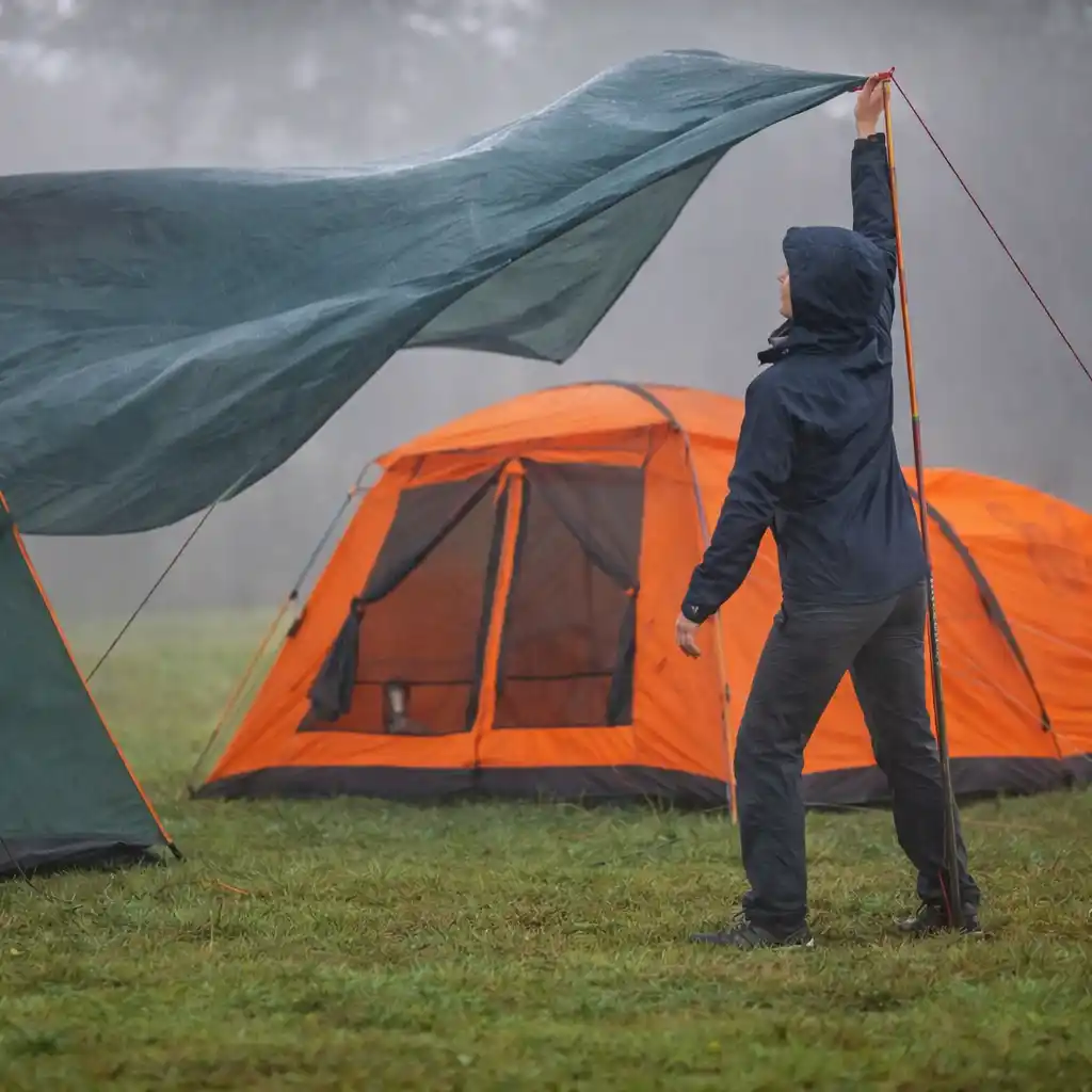 person staking tent ground and tensioning guylines in windy conditions
