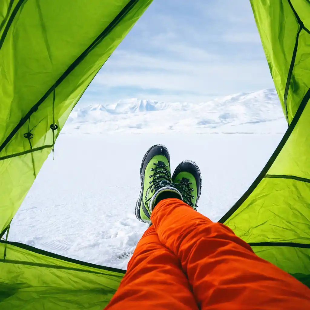 view from inside lime green winter tent with orange pants and mountaineering boots on snow