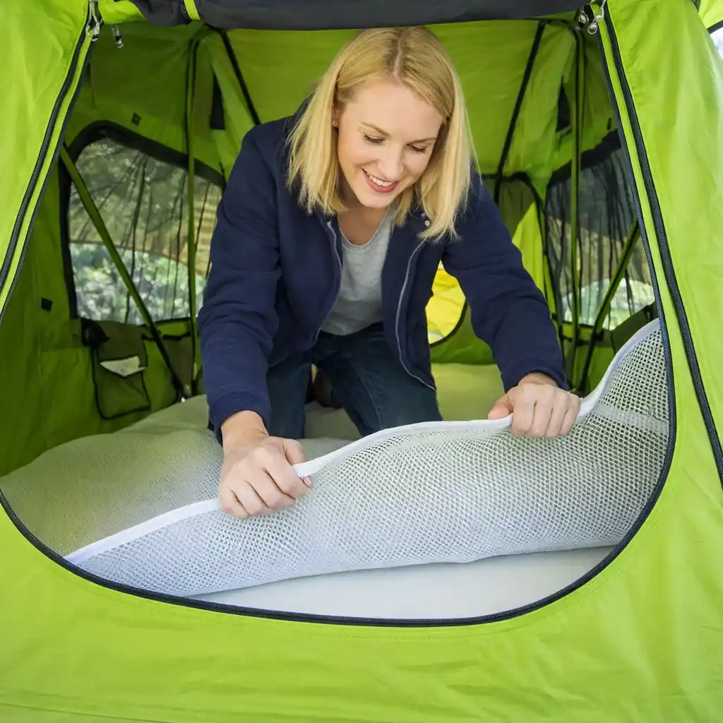 Blonde woman inside a bright lime-green tent adjusting a white mesh sleeping pad