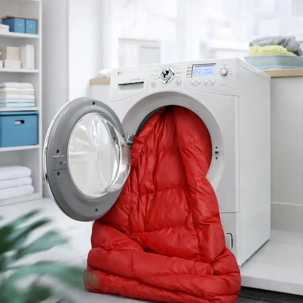 Red sleeping bag being washed in a front-loading washing machine, illustrating proper cleaning and maintenance to restore warmth and insulation over time.