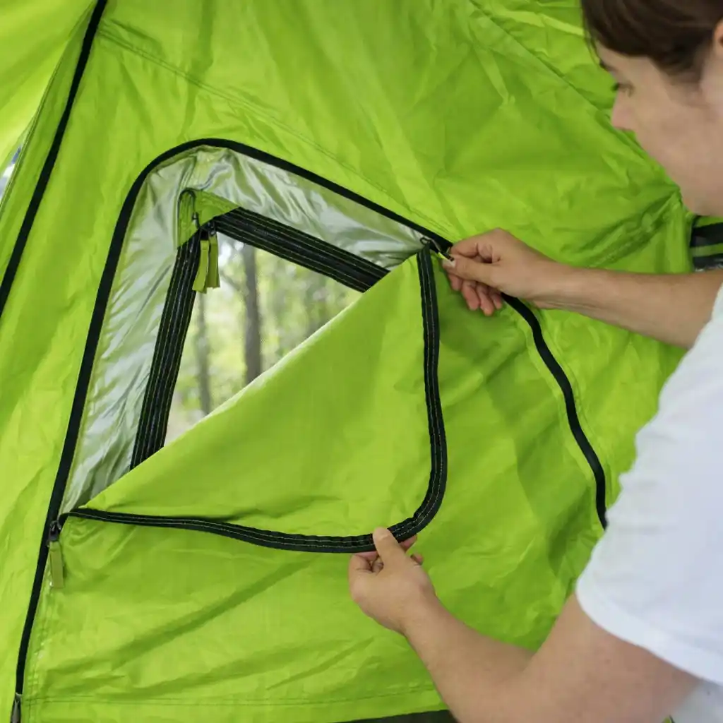 Woman opening the flap of a bright lime-green tent to adjust the mesh window