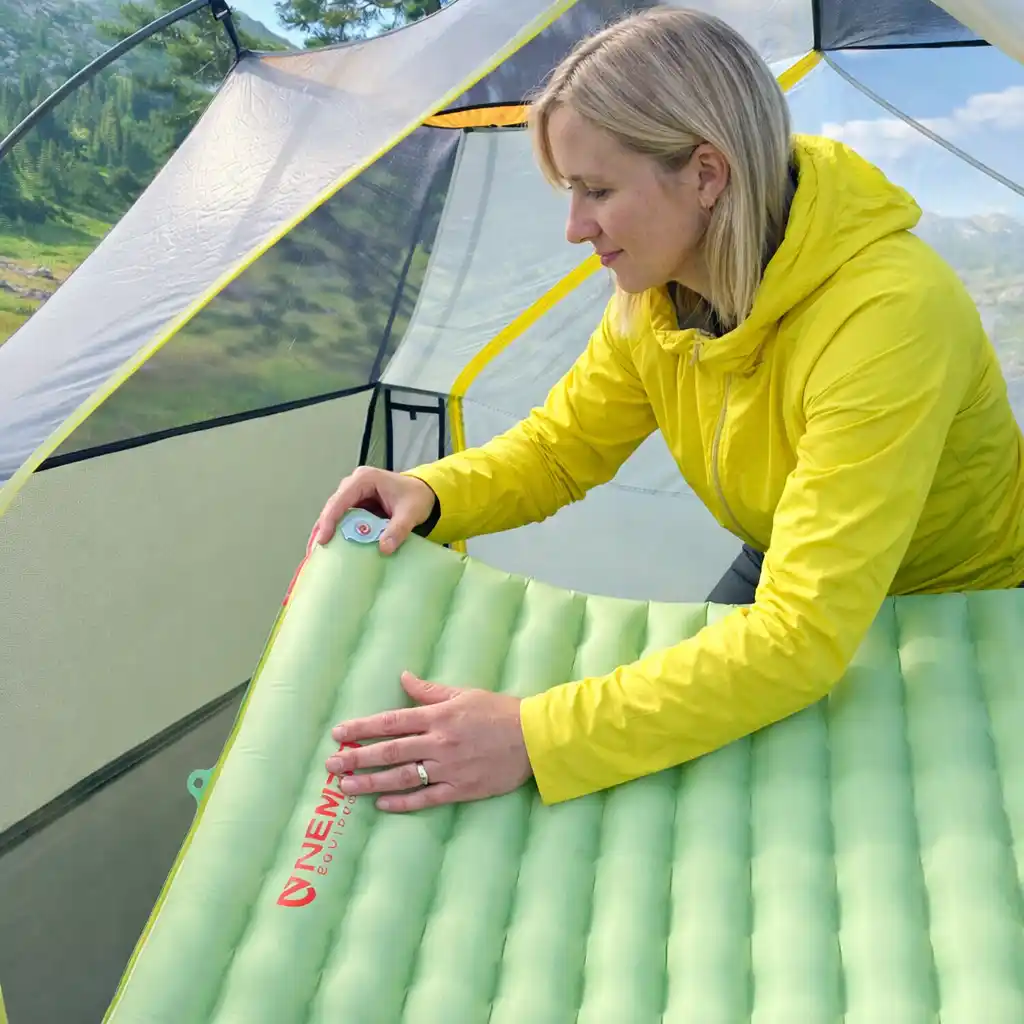 blonde woman setting up an inflatable sleeping pad inside a camping tent