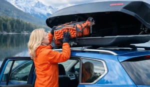 Blonde woman loading gear into roof cargo box on blue SUV