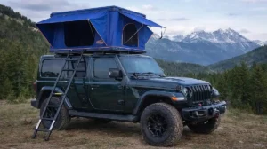 dark green jeep with blue rooftop tent overlanding setup in mountains