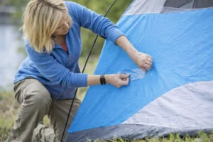 Woman repairing a torn camping tent with repair tape in the field, fixing orange tent fabric damage outdoors