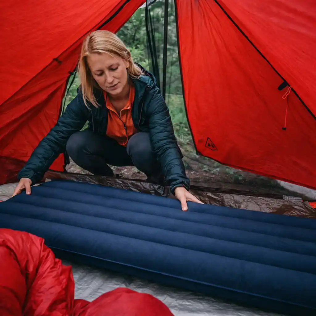 woman placing wide sleeping pad inside red tent showing limited usable space