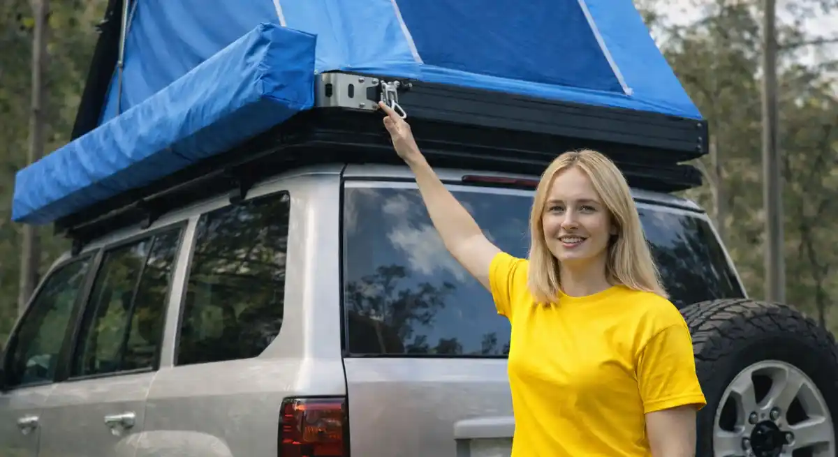 Blonde woman installing a blue rooftop tent on an SUV showing safe mounting position and weight balance