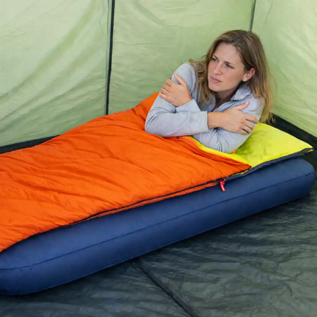 Woman in sleeping bag inside tent hugging herself from cold early morning temperature drop
