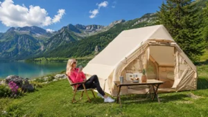 Inflatable camping tent beside a mountain lake with a woman relaxing in a chair during a sunny family camping trip