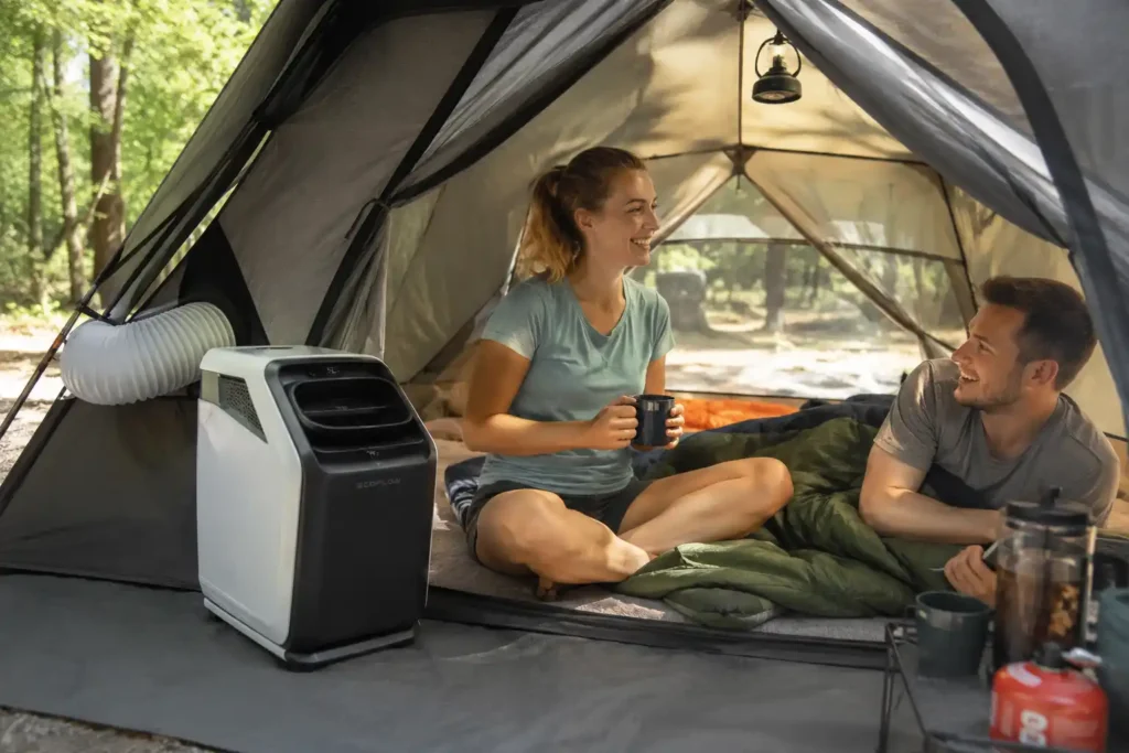 Portable air conditioner cooling the inside of a camping tent while a couple relaxes during a sunny summer camping trip.